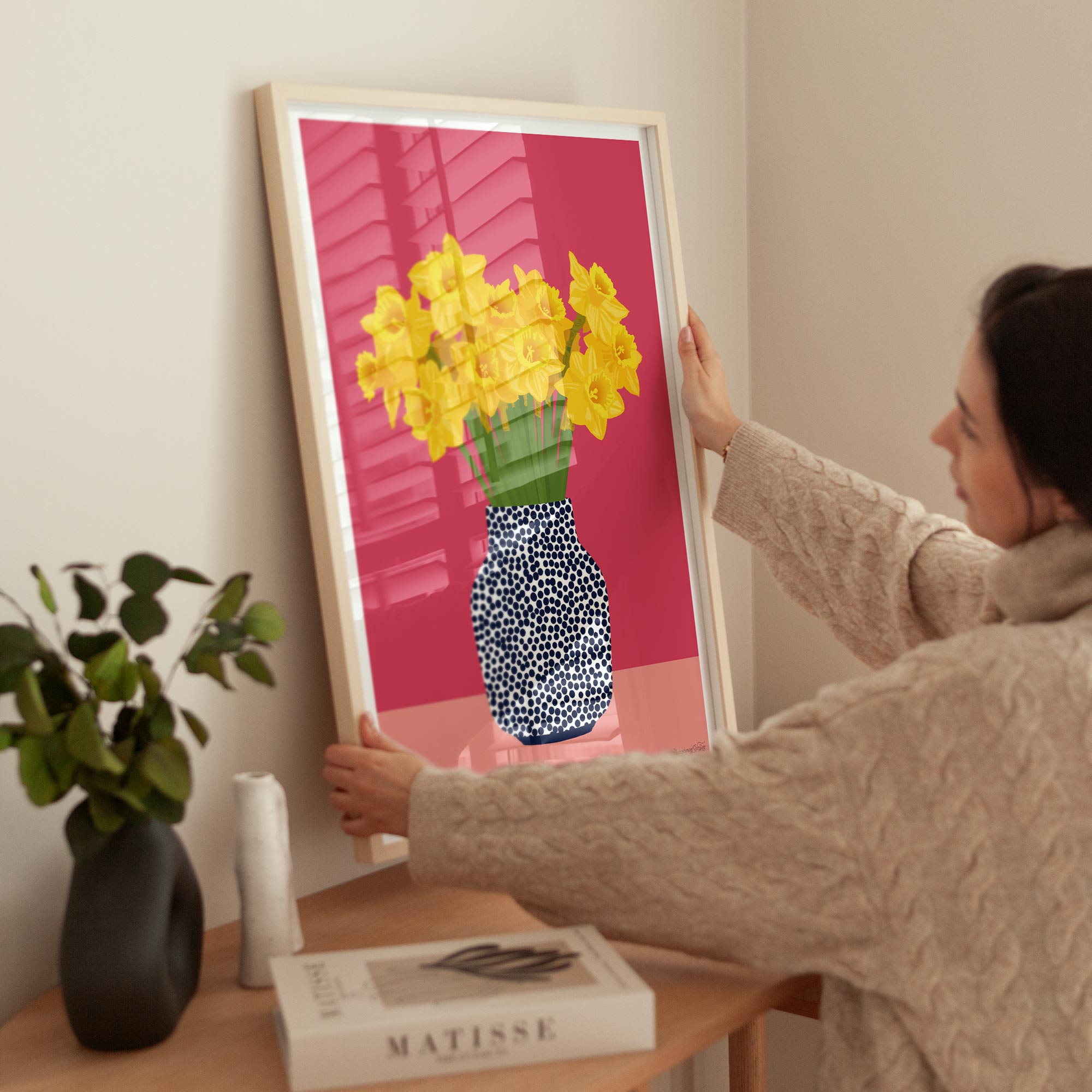 Person hanging a framed artwork of yellow flowers on a pink background