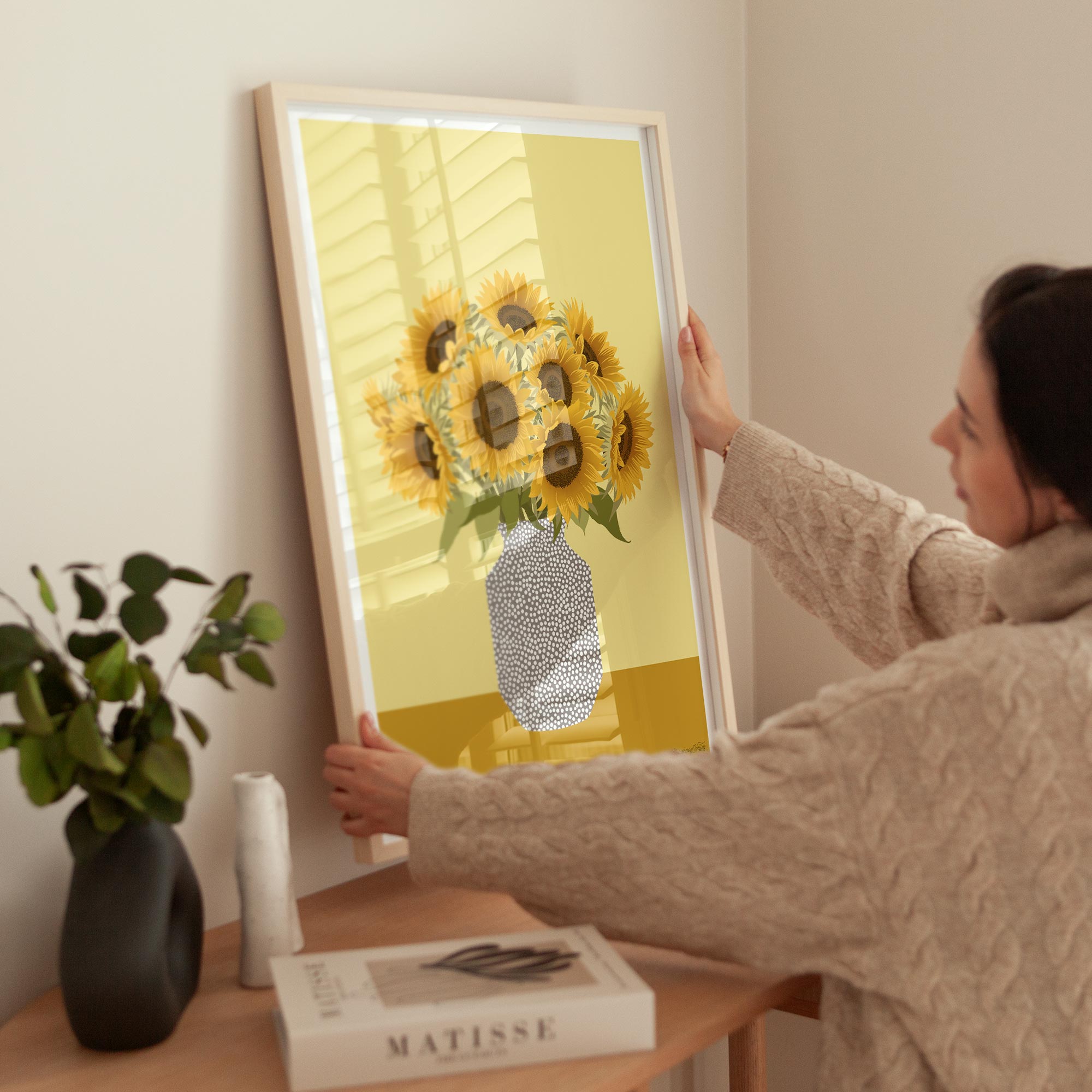 Person holding a framed artwork of sunflowers in a room with decor elements.