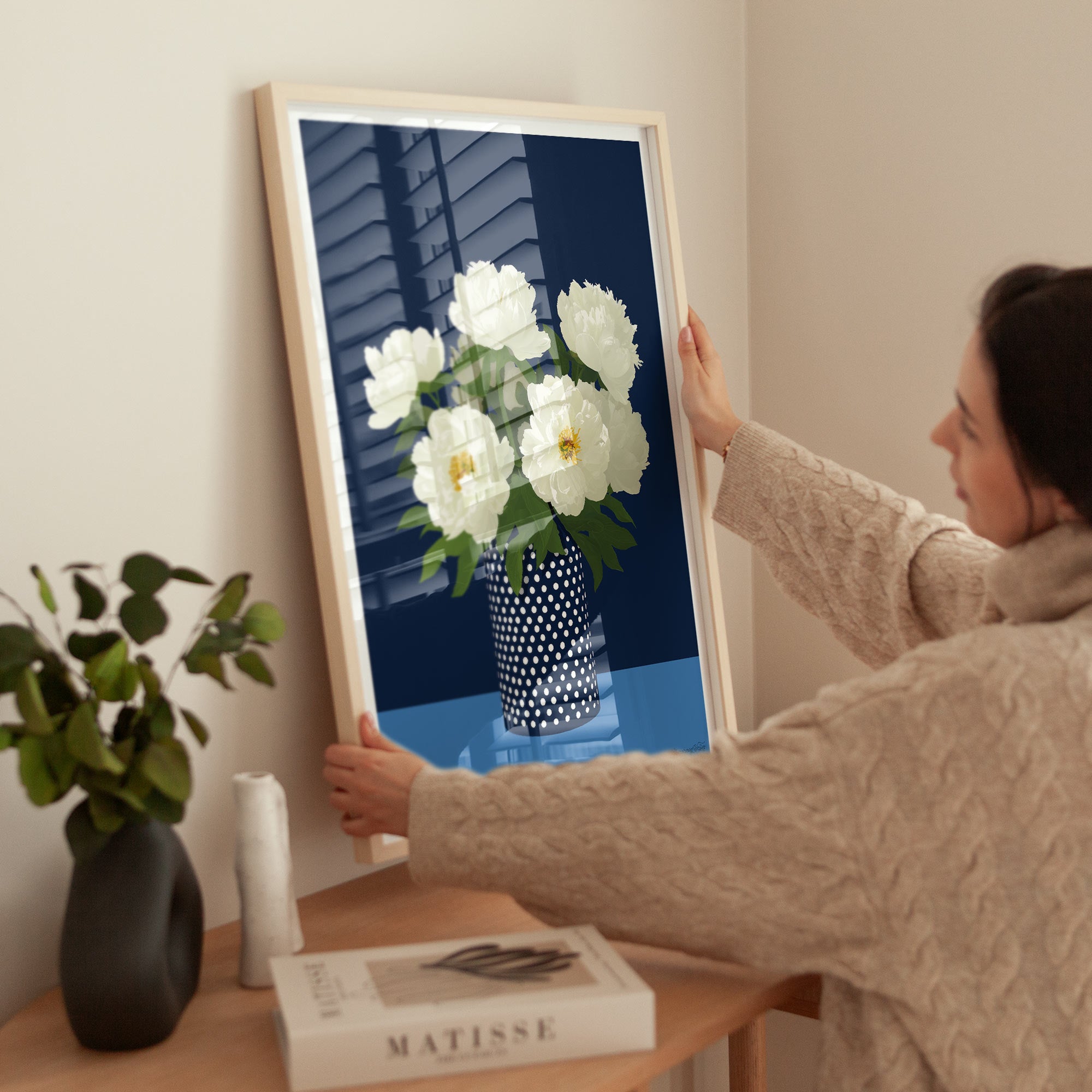 Person holding a framed picture of white flowers in a room with decor elements.