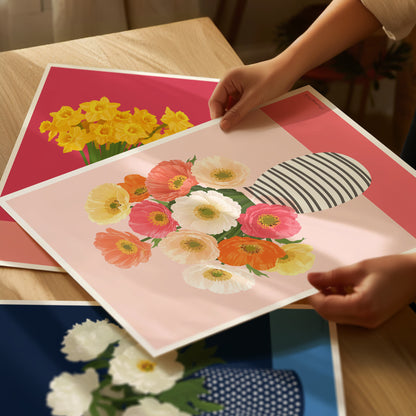 Floral art prints on a table with hands holding one of them.