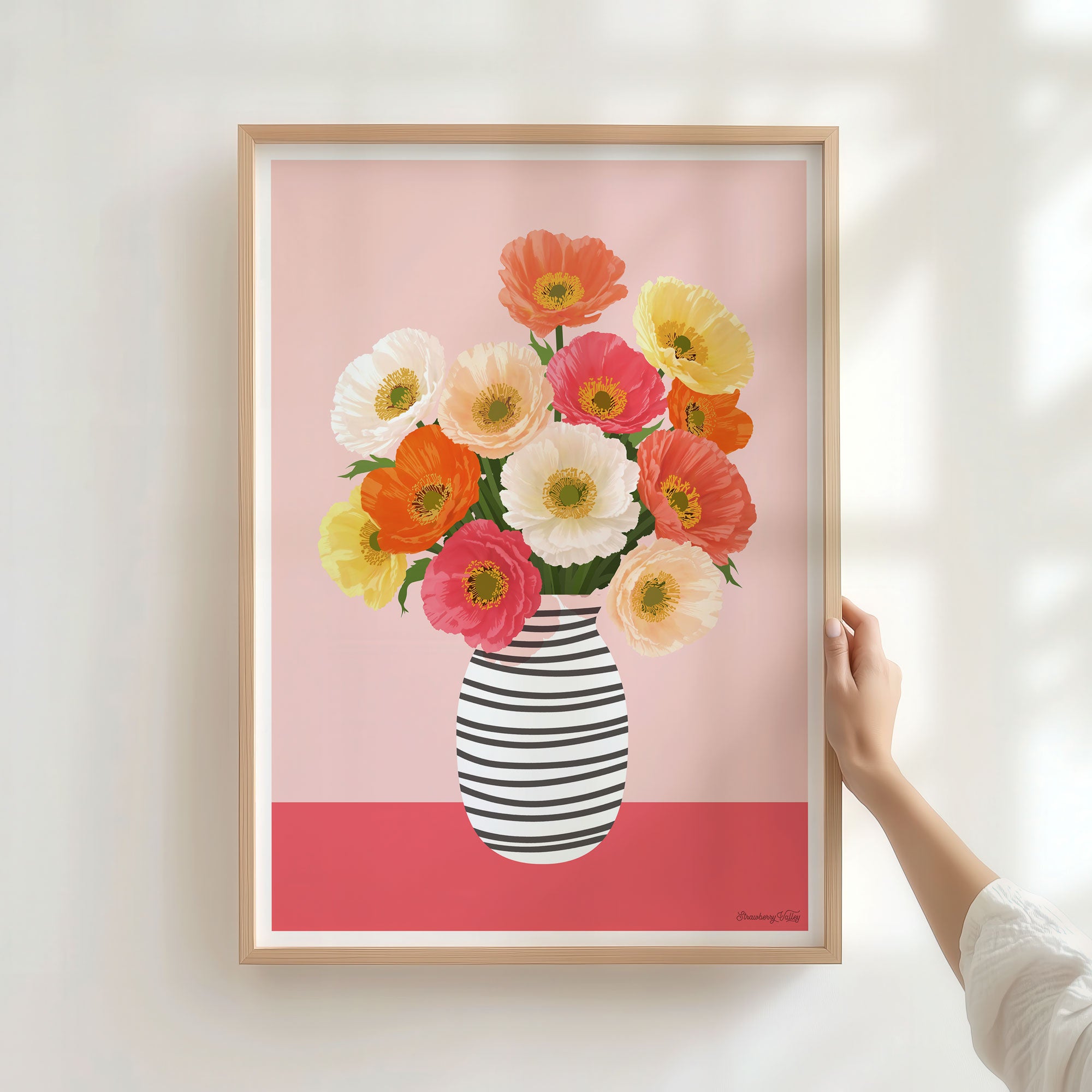 Framed artwork of a colorful floral arrangement in a striped vase on a pink background.