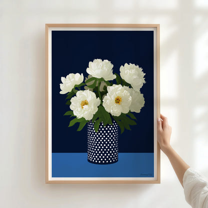 Framed artwork of white flowers in a polka dot vase against a dark blue background.